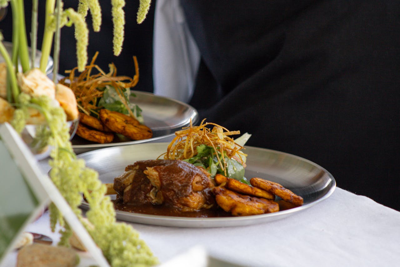 A delicious gourmet dish with meat, fried plantains, and greens, served on a silver platter.